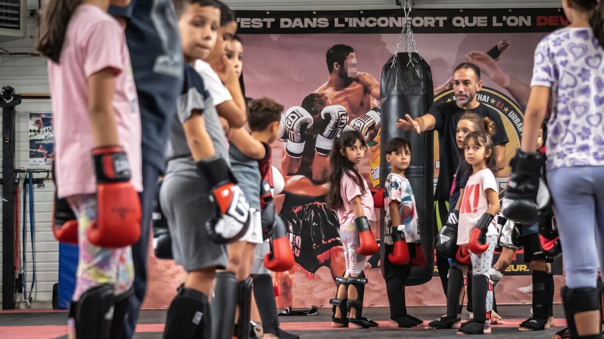 Cours de sport de combat enfants chez Team Ezbiri a Villeurbanne : groupe d enfants en gants de boxe et protege-tibias autour du coach